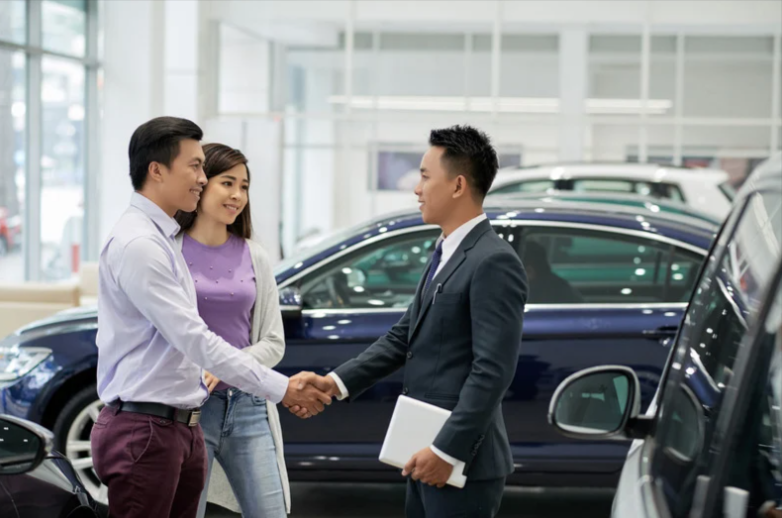 A car salesman shaking hands with a couple who have purchased a new car.